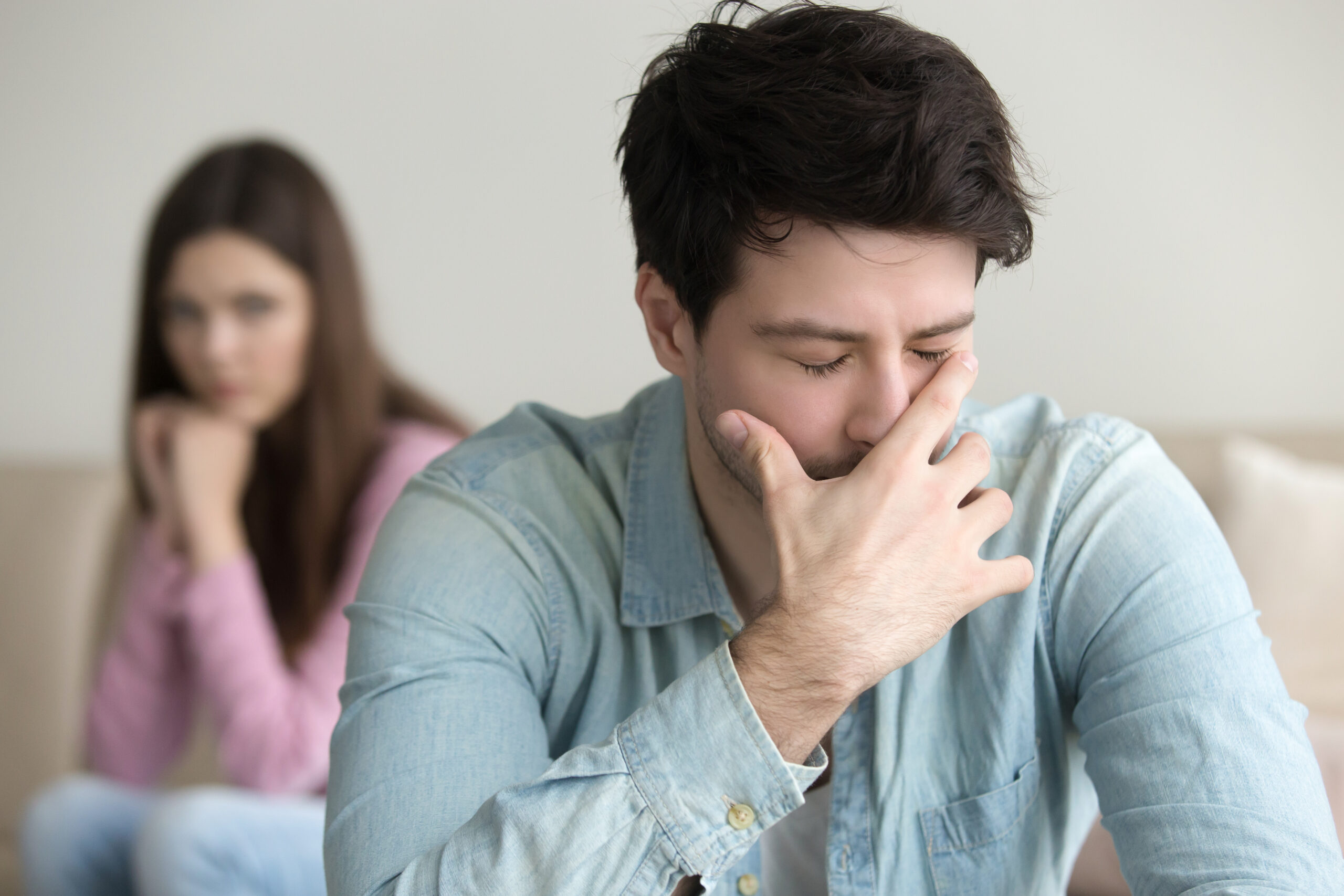 A man sits on a sofa, looking distressed while a woman appears upset capturing the emotional tension of those wondering how to mend a relationship breakdown.