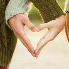 Two people wearing jumpers form a heart shape with their hands, symbolising connection and love, a perfect image for online couples therapy.