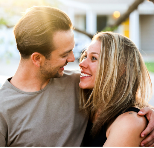 A couple stand close together outdoors, smiling warmly at each other reflecting the happiness they’ve found through online couples therapy.