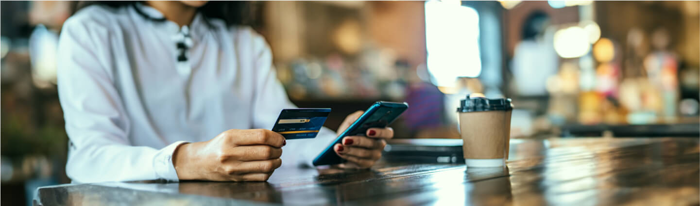 A person sits at a wooden café table, holding a credit card and mobile phone getting ready to sign up for online couples' therapy