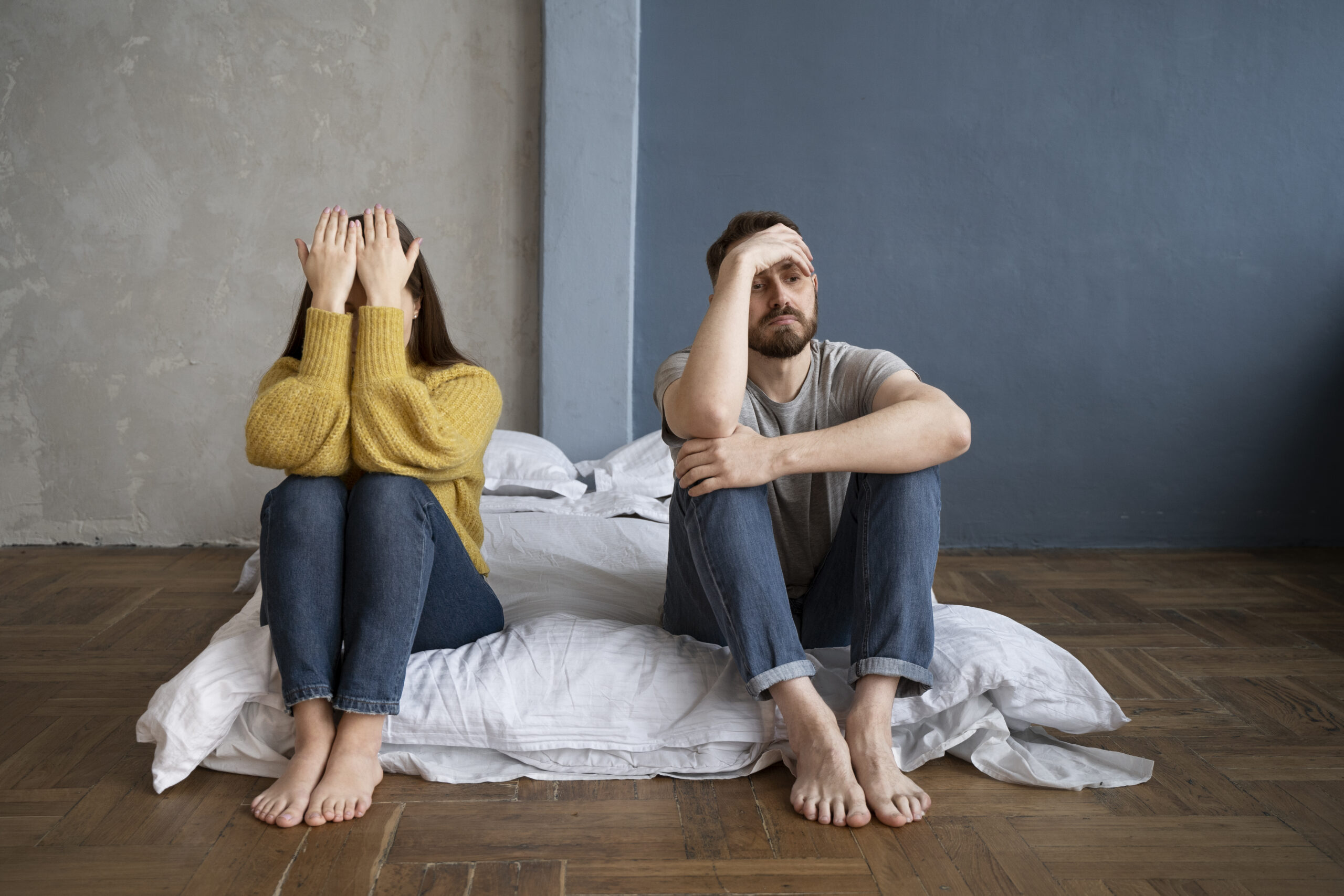A man and woman sit barefoot and distressed on the edge of a bed, reflecting the struggles that can bring couples to seek marriage counselling in Kent