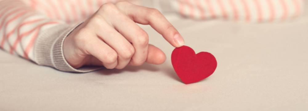 A person gently touches a small red paper heart on a light surface, symbolising the need for counselling for relationship break-ups.