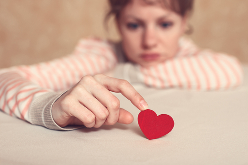 A person with a sad expression gently touches a small red paper heart on a table, symbolising the need for counselling for relationship break-ups.
